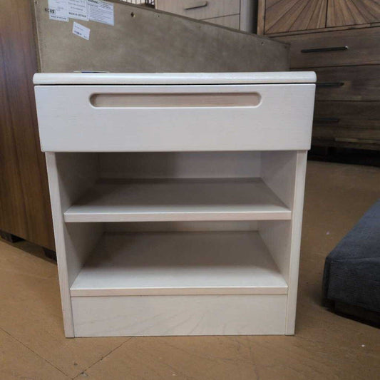 White wooden nightstand with a drawer and shelves in a room setting.