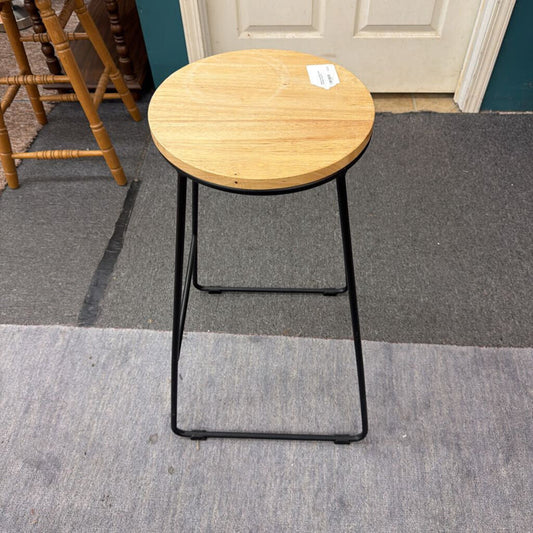 Wooden stool with black metal legs on a gray carpeted floor.