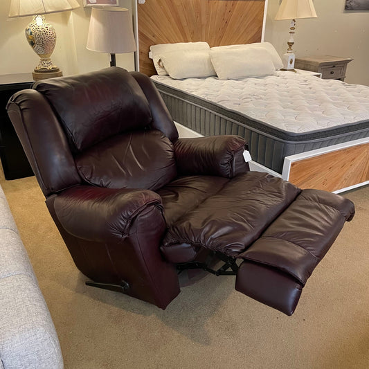 Brown leather recliner chair in a bedroom setting with a bed and lamps.