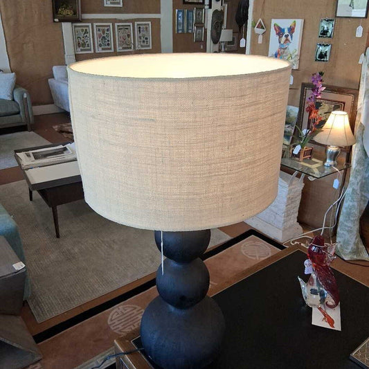 Lamp with beige shade on a table in a room with furniture and decor.