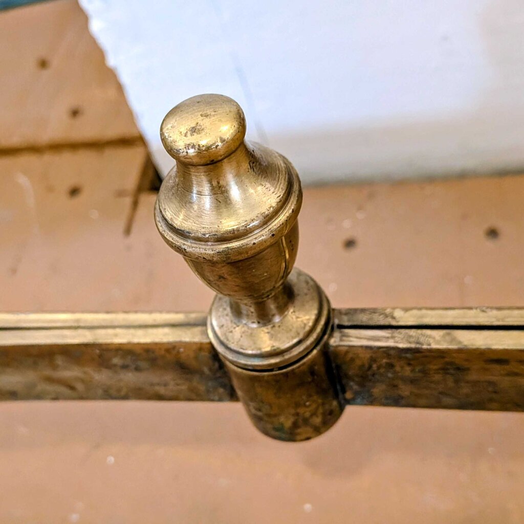 Close-up of a brass bed post on an old wooden bed frame.
