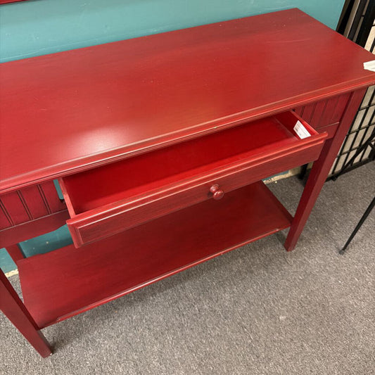 Red wooden desk with a drawer on a gray floor against a teal wall.