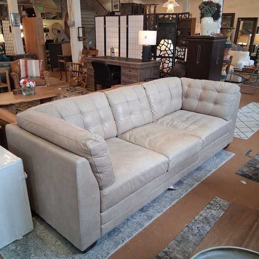 Beige sectional sofa in a furniture store setting with various decor items.
