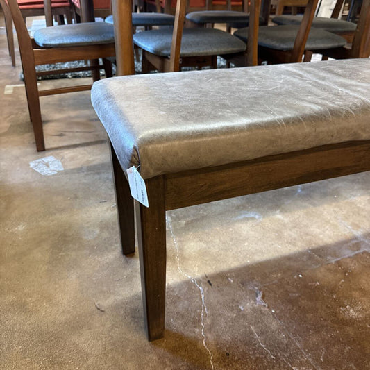 Wooden bench with a textured cushion on a concrete floor, surrounded by chairs.