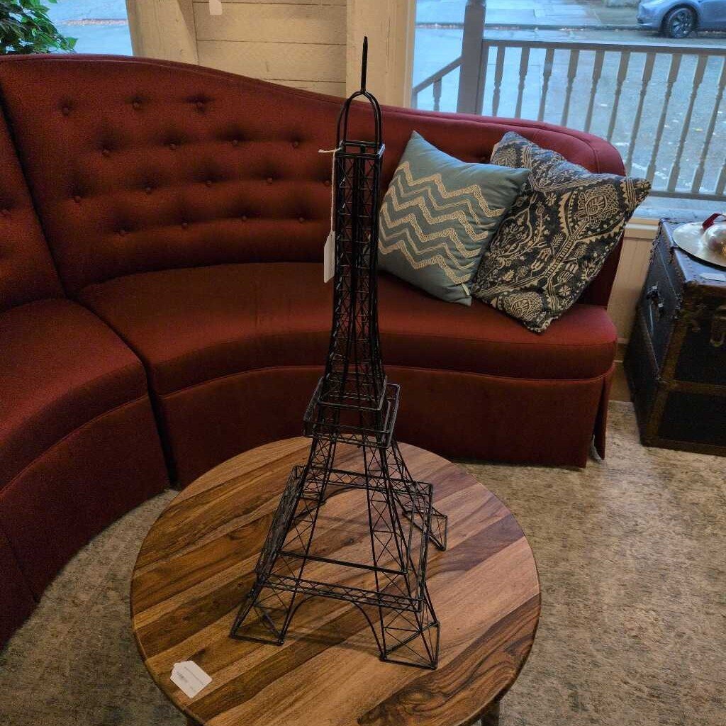 Wireframe Eiffel Tower model on a wooden table with a red sofa and decorative pillows in the background.
