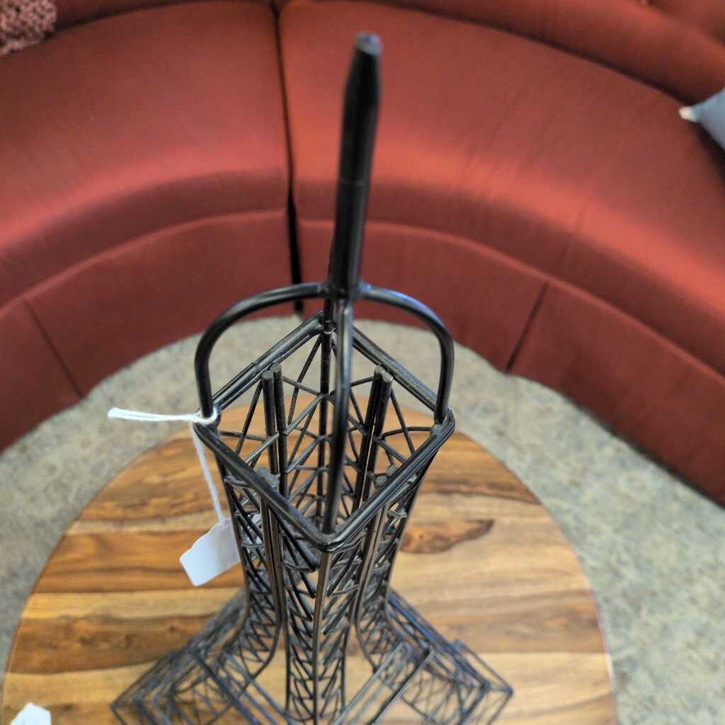 Metallic sculpture of a tower on a wooden surface with a red upholstered chair in the background