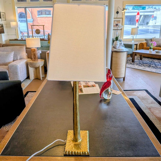 Table lamp with a gold base and white shade on a table in a living room setting.
