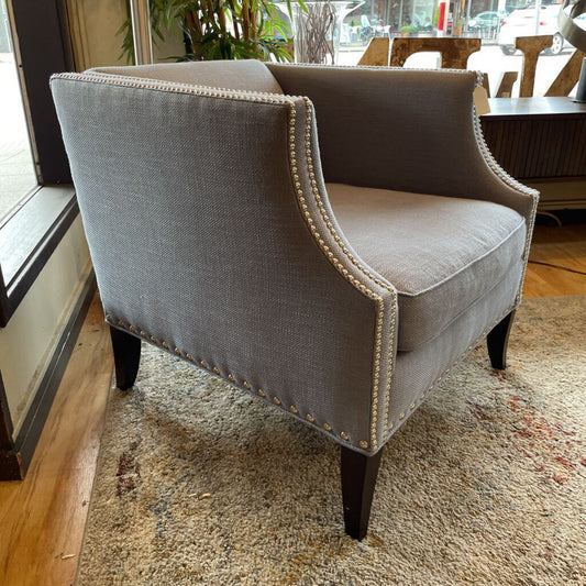 Gray upholstered chair with nailhead trim on a carpeted floor.