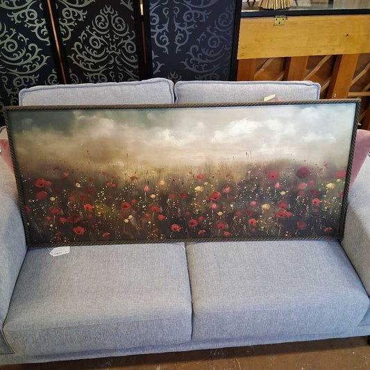 Gray sofa with a large framed painting of a floral field on a wooden floor.