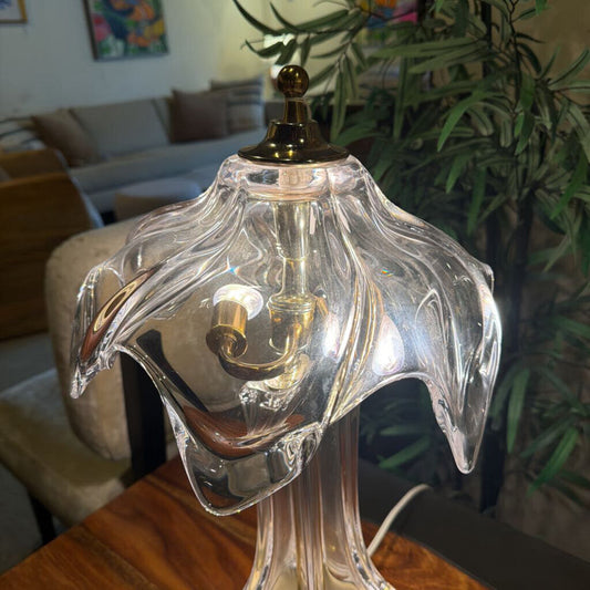 Clear glass lamp with gold base on a wooden surface, blurred indoor background
