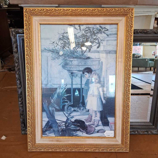 Framed artwork of two children by a fireplace with decorative elements.