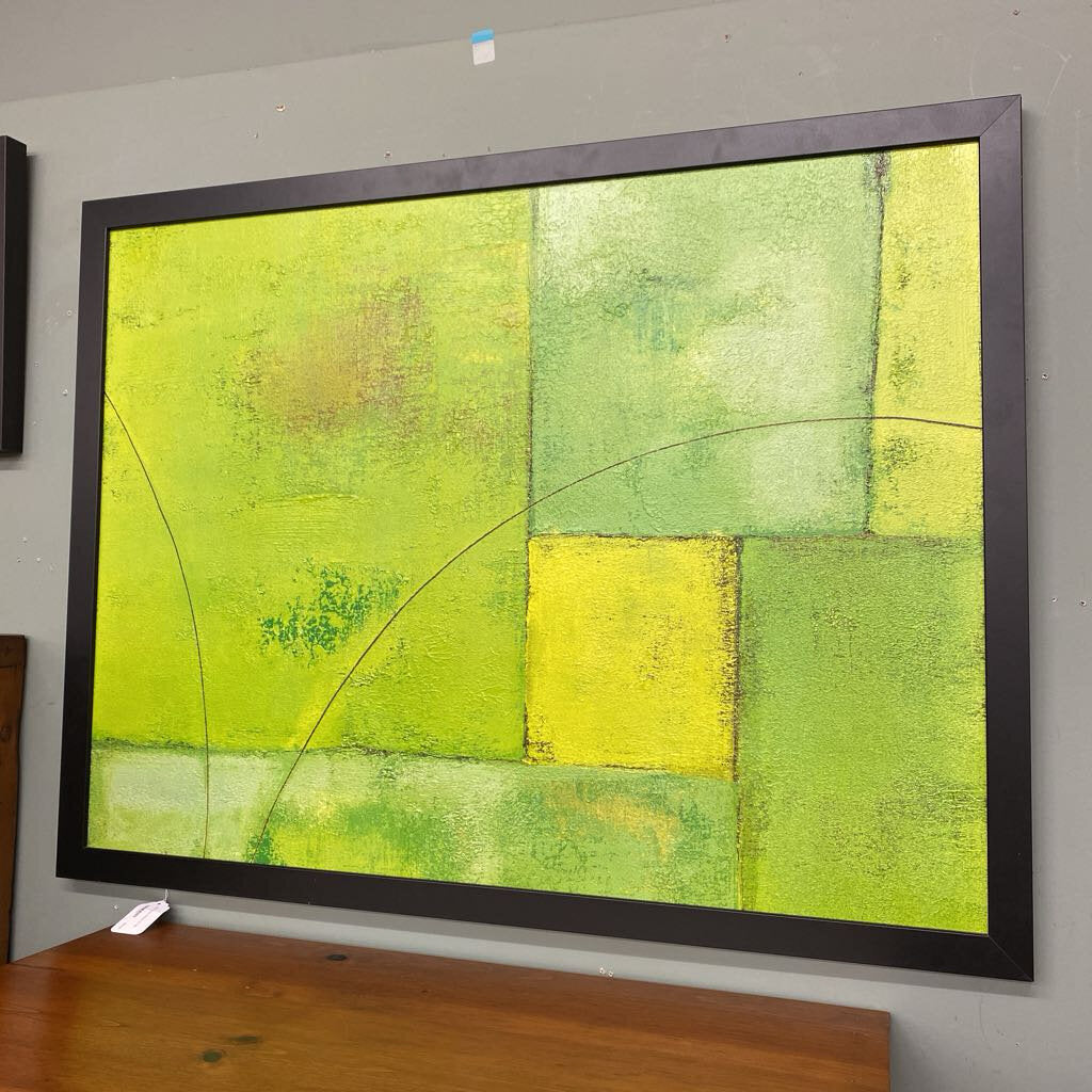 Abstract art piece with green and yellow colors in a black frame on a gray wall.