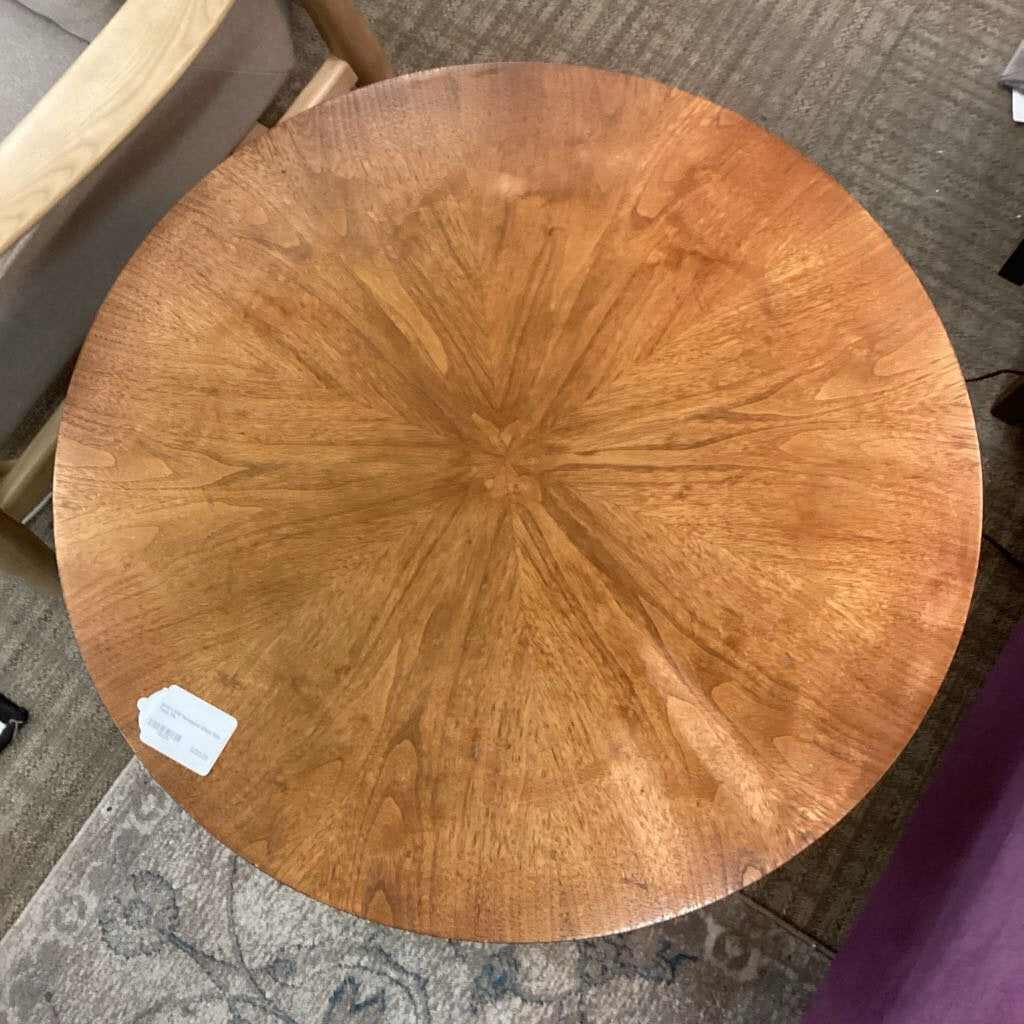 Round wooden table top with a visible brand label on a carpeted floor.