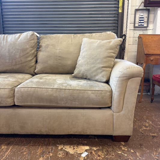 Beige sofa with visible wear in a room with a wooden floor and a metal shutter.