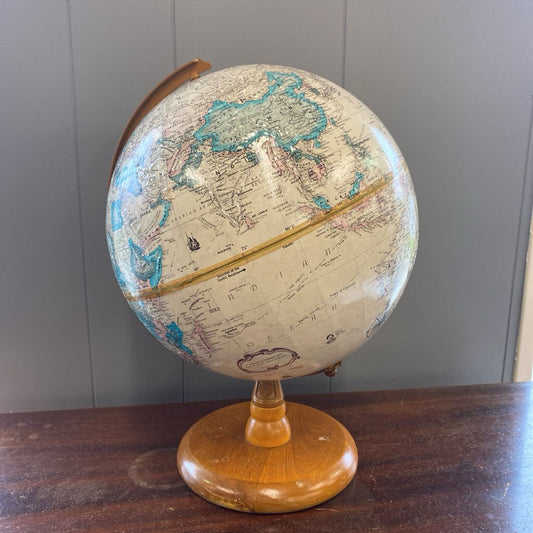 Vintage-style globe on a wooden stand against a gray wall.