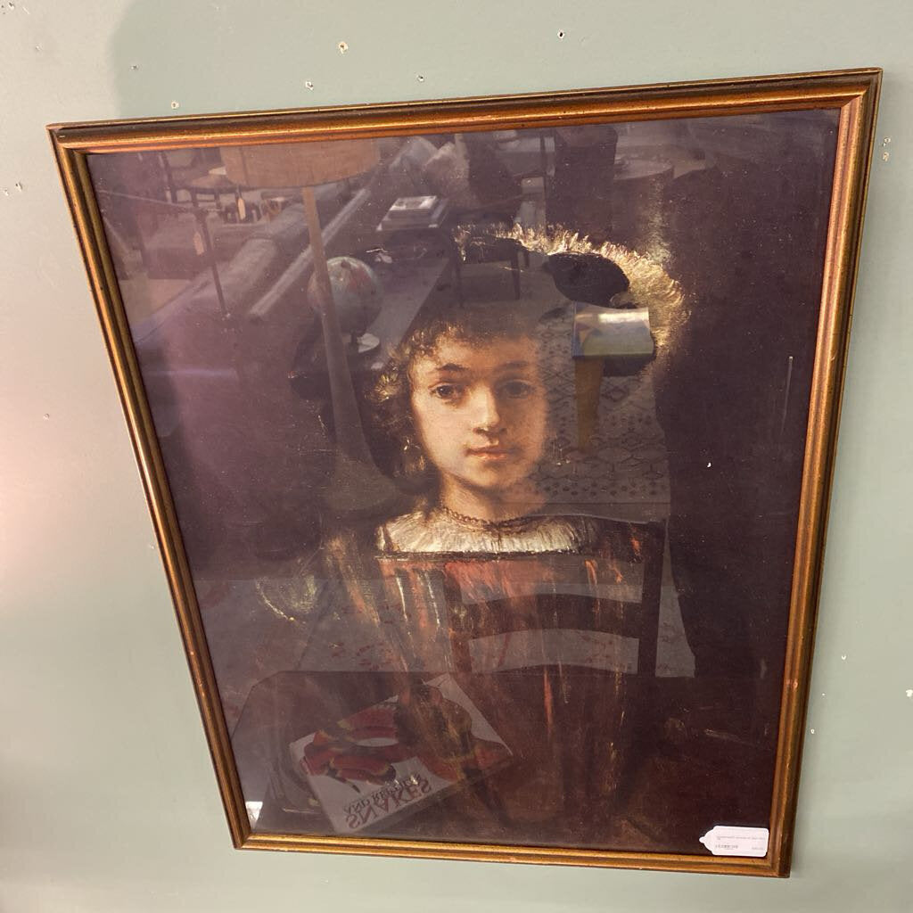 Framed portrait of a young girl with a gold frame on a light gray wall.