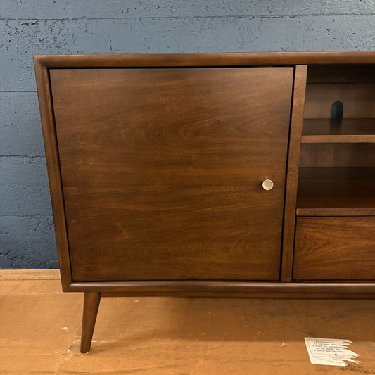 Wooden cabinet with a single door and shelf against a blue wall.