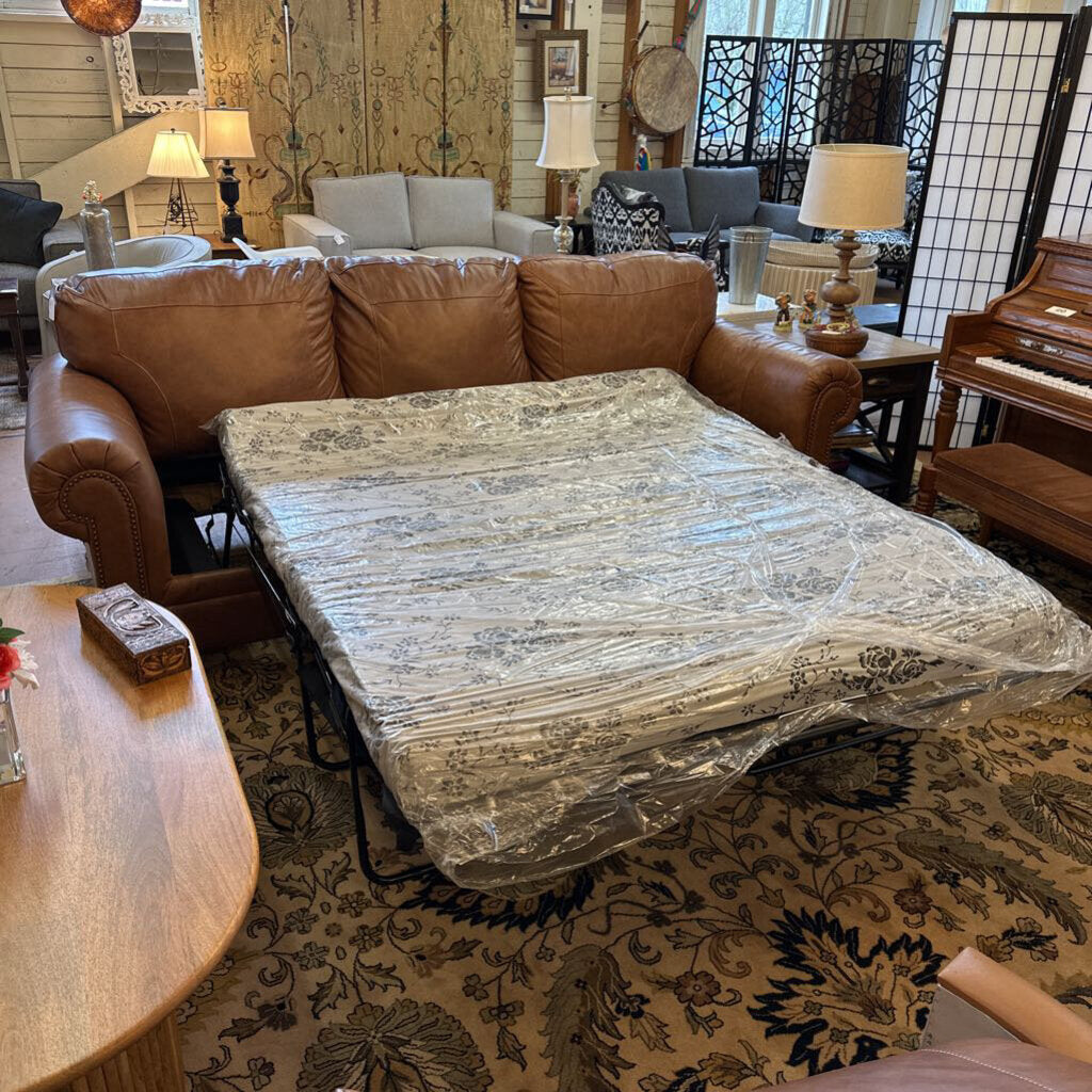 Brown leather sofa with a mattress on top in a room with decorative elements.