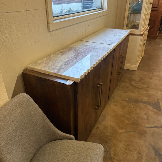 Wooden cabinet with marble countertop next to a window in a room with brown carpet.
