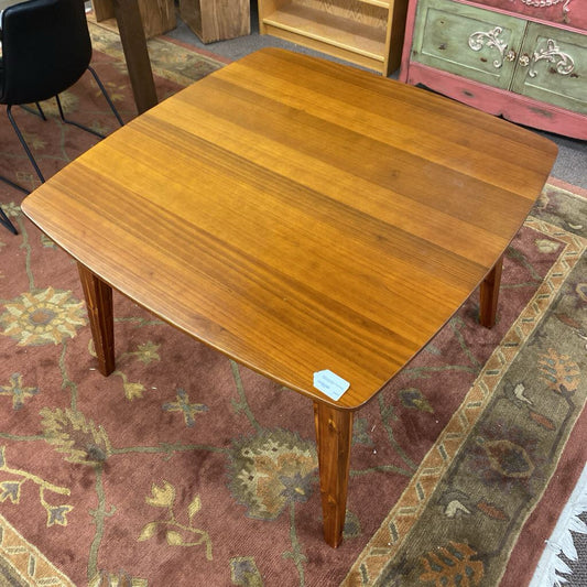 Wooden table on a patterned rug with a chair and cabinet in the background