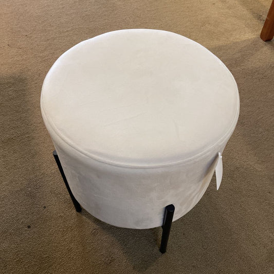 White round ottoman with black legs on a beige carpet