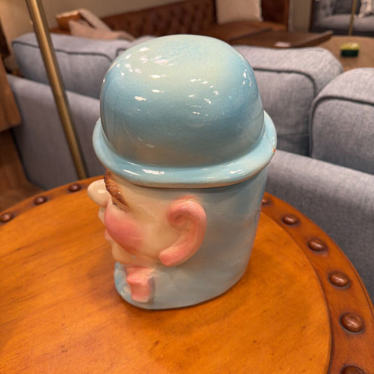 Ceramic mug shaped like a cartoon character with a blue lid on a wooden table.