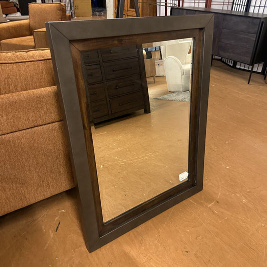 Rectangular mirror with a dark frame on a wooden floor, surrounded by furniture.