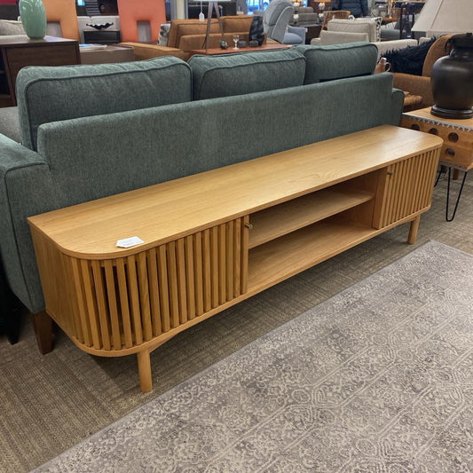 Wooden TV stand in front of a green sofa on a patterned carpet