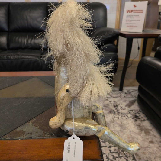 Decorative gnome figure with long hair on a wooden stand in a room with black leather furniture.