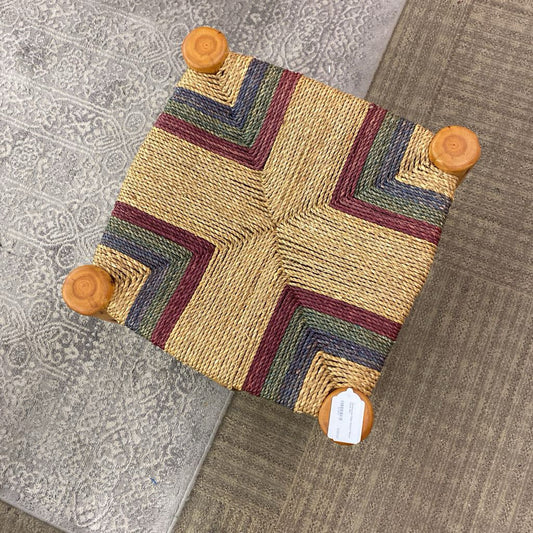 Small woven stool with a geometric pattern on a textured floor.