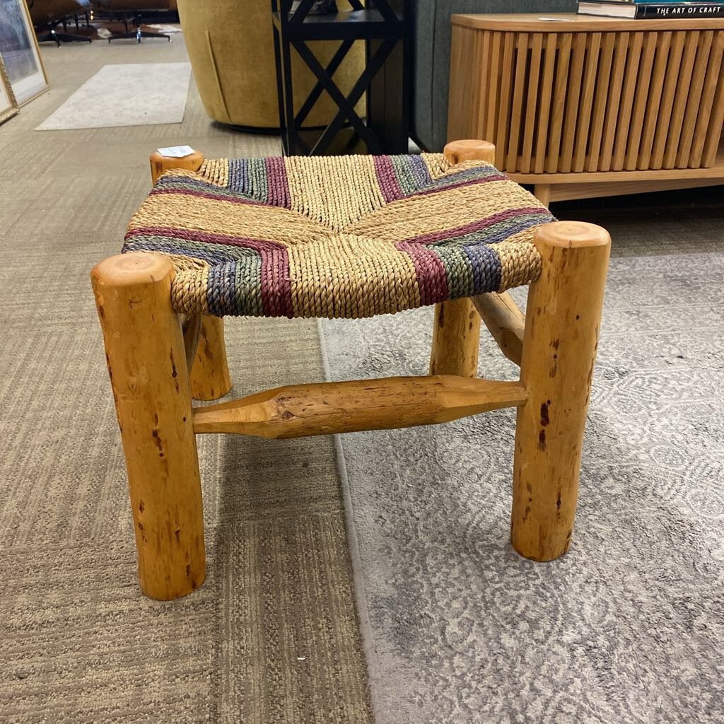 Wooden stool with a multicolored woven seat in a room setting.