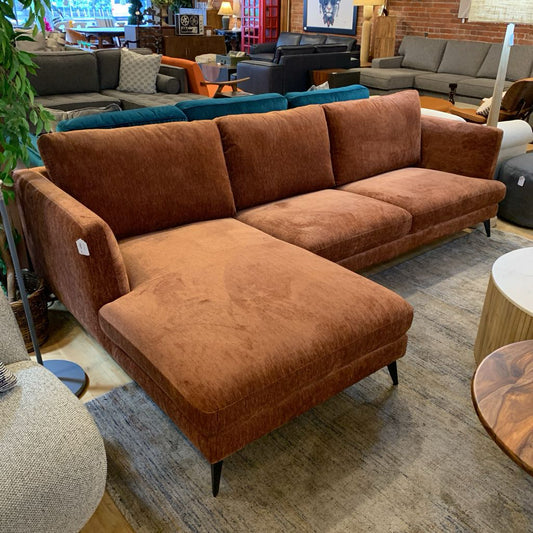 Brown sectional sofa in a showroom setting with other furniture and decor.