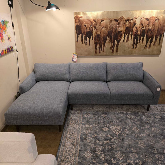 Gray sectional sofa in a room with a large painting of cows on the wall.