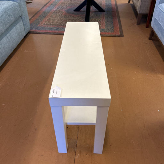 White rectangular table on a wooden floor with a gray couch in the background