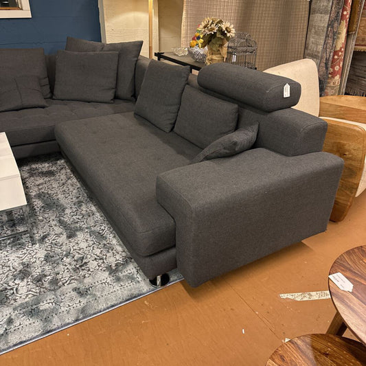 Gray sectional sofa in a showroom setting with a rug and other furniture items.