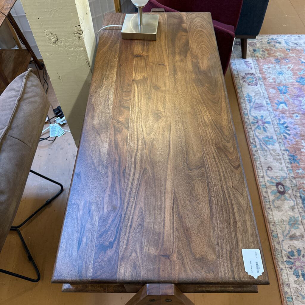 A slim, dark wood writing desk with a minimalist rectangular top, two open storage cubbies, and angled A-frame legs, shown on a neutral carpet.