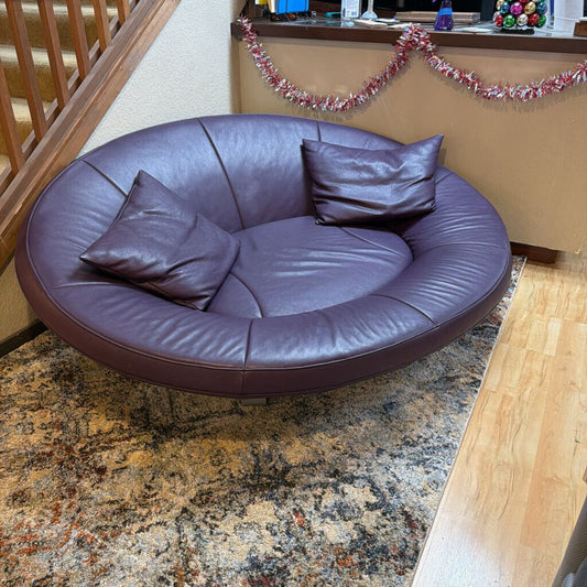 Round purple leather sofa with cushions on a patterned rug.