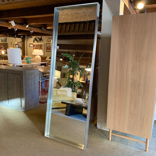 Large floor mirror reflecting a room with furniture and decor.
