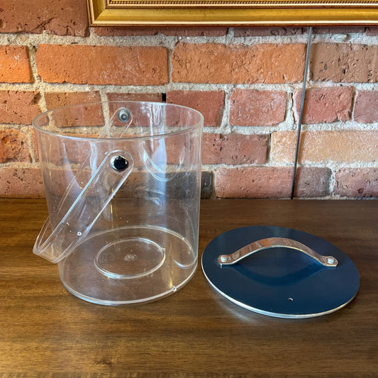 Clear plastic container with a blue lid on a wooden surface against a brick wall.