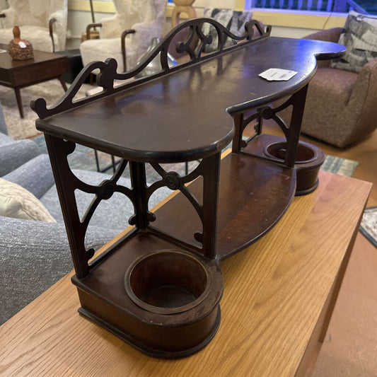 A dark-stained wooden antique vanity shelf or desk organizer featuring an ornate fretwork gallery and two circular recessed wells on the base, sitting atop a modern light oak dresser.