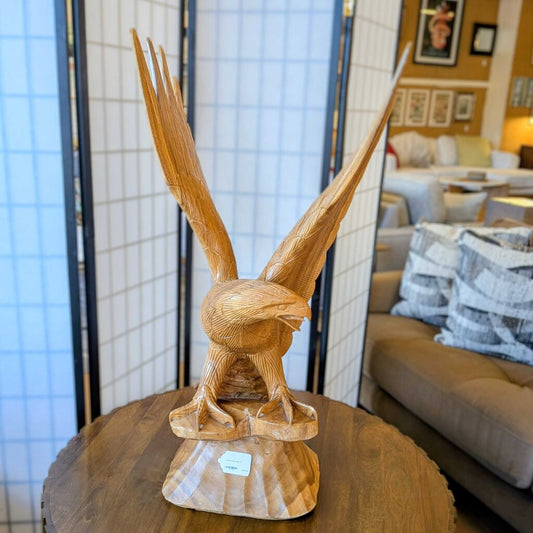 A detailed wooden sculpture of an eagle with its wings spread wide, perched on a carved base on a circular table.