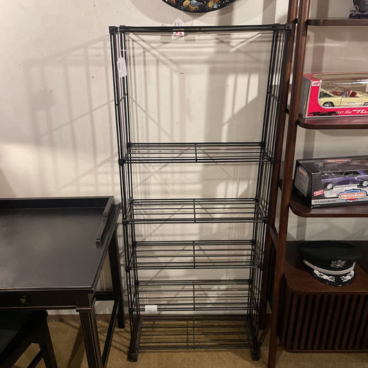 Metal shelving unit against a wall with a table and other items in the foreground.
