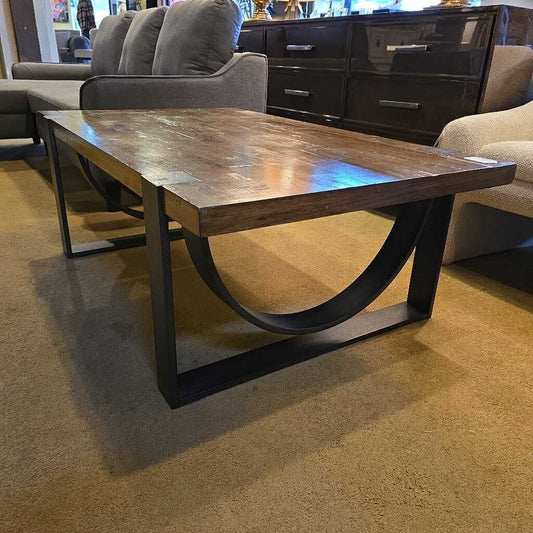 Industrial-style coffee table with a thick, distressed wood plank top and heavy black metal sled legs featuring curved support braces.