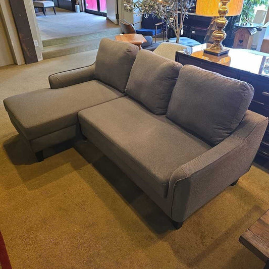 Gray sectional sofa in a living room setting with a lamp and table in the background.