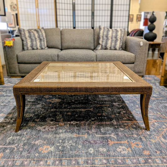 Wicker coffee table in front of a gray sofa with patterned cushions on a textured rug.