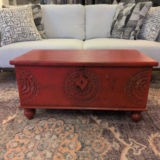 Red wooden chest on a patterned rug with a white couch in the background