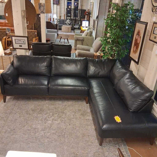 Black leather sectional sofa in a showroom setting with other furniture and decor.