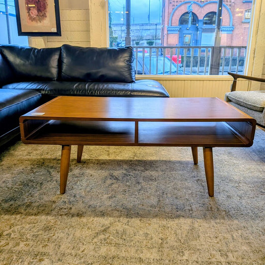 Wooden coffee table in a living room with a black leather sofa and large window.