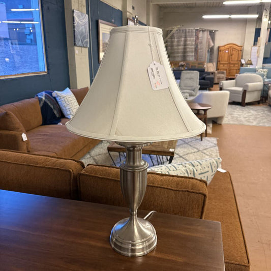 Table lamp with beige shade on a wooden table in a furniture store setting