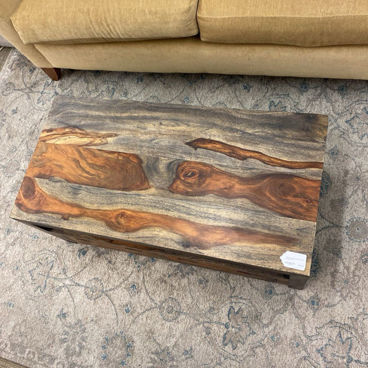 A rectangular solid wood coffee table with a thick top, an open storage shelf, and two drawers, showcasing a vibrant, dark-streaked natural wood grain.